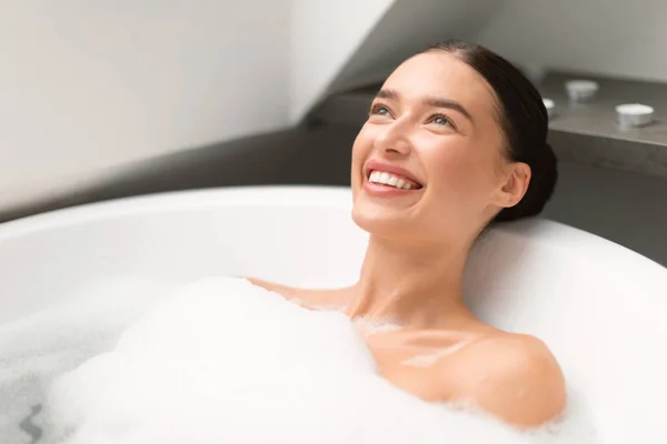 快乐的女士在泡沫泡沫中洗澡 在现代化的浴室里微笑着向上看 女人洗澡和放松室内 美事与宠爱的概念 — 图库照片