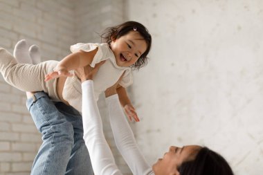 Mutlu Koreli anne, küçük kızıyla oynuyordu. Yatakta bacaklarının üzerinde uzanmış çocuk sürerken eğleniyordu. Anne ve bebek evde kucaklaşıyorlar. Seçici Odaklanma Sevimli Bebek Kız üzerine