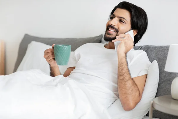 Usmívající Tisíciletý Arabský Muž Plnovousem Leží Posteli Šálkem Kávy Hovorů — Stock fotografie
