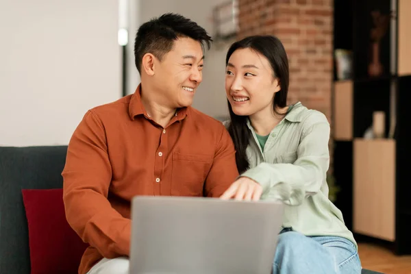 积极的亚洲男子和妇女使用笔记本电脑 网上购物或有视频通话 坐在沙发上的家庭内部 推荐新应用于会议 广告和提供 — 图库照片