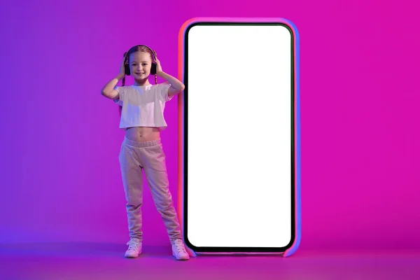 Positive Cheerful Stylish Preteen Girl Wireless Headphones Standing Big Phone — стоковое фото