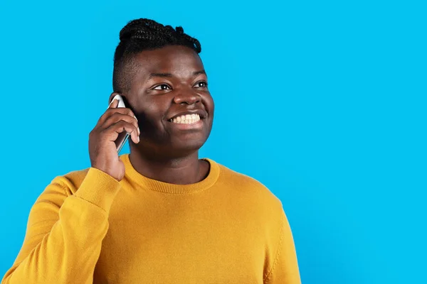移动通信 开开心心的非裔美国人 一边在手机上说话 一边环顾四周 一边站在蓝色的背景上享受着愉快的对话 复制空间 — 图库照片