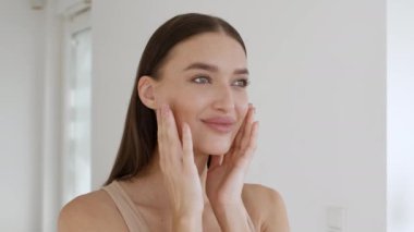 Kadınlık ve doğal güzellik. Genç beyaz bir bayan aynaya bakıyor ve güzelleşiyor, pürüzsüz cilt durumunun tadını çıkarıyor, boş bir alan.