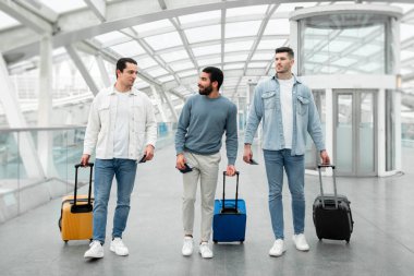 Seyahat bavullu üç erkek turist modern havaalanındaki uçuşlarını terminalde bekliyorlar. Ulaşım ve Ucuz Biletler Teklif Konsepti. Tam Uzunluk Çekimi