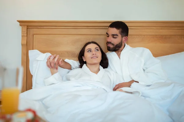 Multiethnic Couple Hugging Lying Bed Hotel Room Enjoying Romantic Vacation — Stock Photo, Image