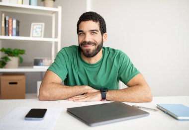 Bin yıllık gülümseyen Arap adam, iş yerinde sakallı, akıllı telefonlu ofis içi boş ekranlı ve dizüstü bilgisayarlı yönetici. İş ve girişim, uzaktan çalışma, serbest çalışma, evde yeni normal