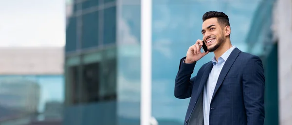 stock image Cheerful successful arab millennial businessman calling by smartphone near building office outdoor, empty space, panorama. Business with gadget, work, new normal and communication