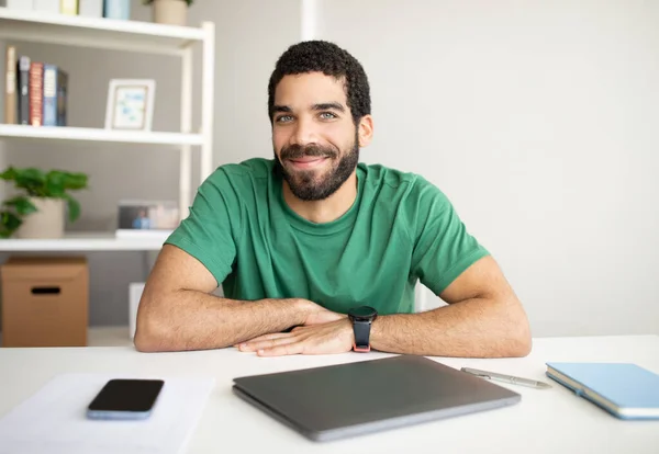 Smiling millennial arab guy manager with beard at workplace with smartphone with blank screen and laptop in office interior. Business and startup, work remotely, freelance, new normal at home