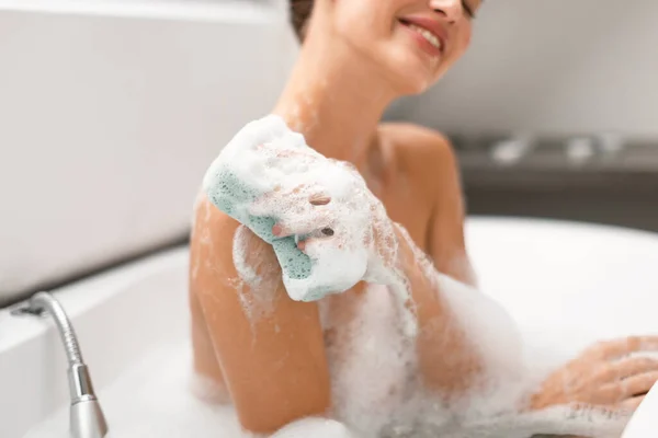 ボディケア バスルームの屋内で泡で水に座ってスポンジで肩をこすり認識できない女性洗濯ボディ 入浴を楽しむ女性の作物のショット 選択的フォーカス — ストック写真