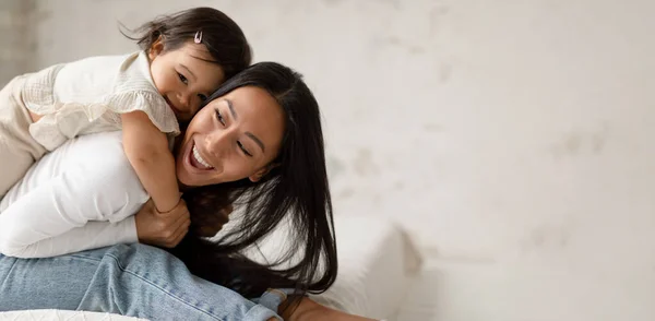 愛らしいアジア系の赤ちゃんの娘は 母親を抱っこし 自宅で楽しい時間を過ごしています 幸せな母と幼児幼児幼児の女の子はベッドルームで接着し 笑っています テキストのための空のスペースを持つパノラマ — ストック写真