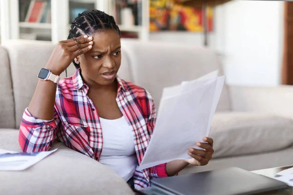 驚くべき動揺若い黒人女性が自宅でソファで床に座って 紙を保持し 女性の独立した請負業者は 通信を読んで 彼女の頭に触れ 悪いニュースを持っている スペースをコピー — ストック写真