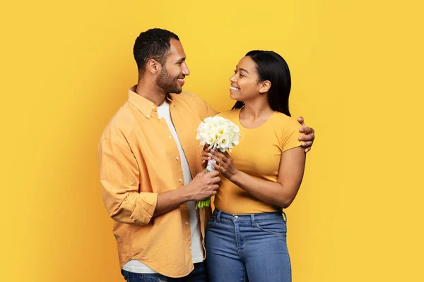 快乐的千年非洲裔美国丈夫送给妻子一束鲜花和拥抱 祝贺他们的生日 周年纪念日在黄色的工作室背景下被隔离 爱情和约会 — 图库照片