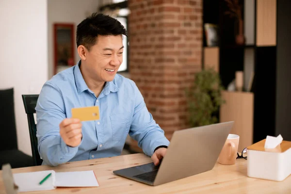 亚洲中年男子坐在笔记本电脑前 拿着信用卡 凭账户 总公司内部 复制空间检查钞票 财务经理 自由职业 网上购物 — 图库照片