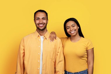 Sarı stüdyo arka planında izole edilmiş kameraya bakarak binlerce yıllık gülümseyen Afrikalı Amerikalı çiftin portresi. İlişkiler, aşk, yaşam tarzı, reklam ve teklif