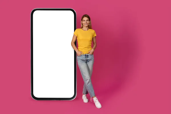 广告和报价 快乐而自信的成熟的欧洲金发女性 随意站在巨大的智能手机旁边 屏幕空旷 背景是粉色的工作室 App Website Blog Lifestyle — 图库照片