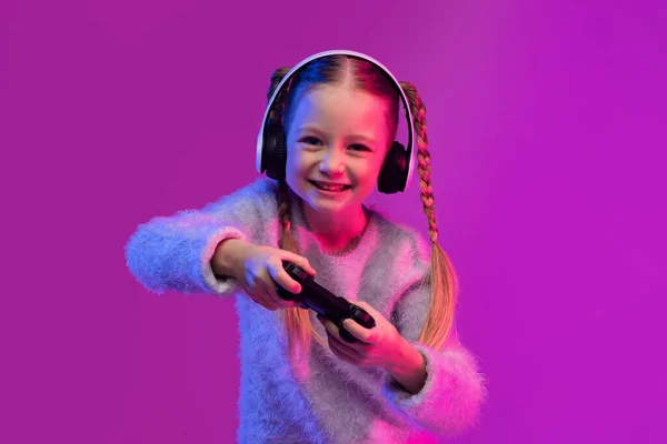 快乐甜美的金发少女在霓虹灯下玩彩色背景的电子游戏 用无线耳机和手握操纵杆 儿童游戏成瘾概念 — 图库照片