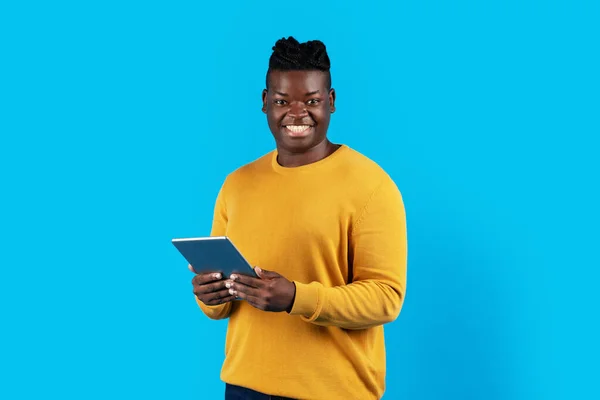 微笑着拿着数码记事板的黑人年轻人 看着相机 快乐的千年黑人男性用现代小工具上网购物或做远程工作 蓝色背景 复制空间 — 图库照片