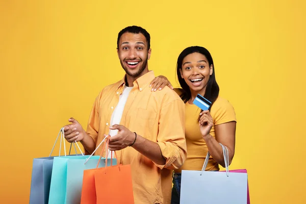 令人高兴的是 千禧年的非洲男男女女带着许多包裹 推荐用信用卡购物 享受在黄色工作室背景下一起购物的乐趣 退还现金 — 图库照片