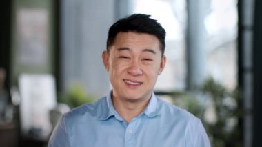 Ofis çalışanı. Kameraya gülümseyen, hafif modern kurumsal iç mekâna poz veren, ağır çekimde pozitiflik gösteren orta yaşlı Asyalı adam yöneticisinin yakın portresi.
