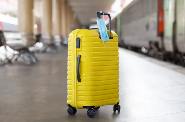 stock image Yellow Luggage Suitcase With Hanged Protective Medical Face Mask Standing Abandoned On Platform At Railway Station, Conceptual Image For Safe Travels During Coronavirus Pandemic, Copy Space