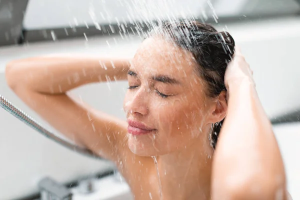Pretty Lady With Eyes Closed Taking Shower Washing Head Under Falling Water In Modern Bathroom Indoors. Woman Enjoying Haircare Routine. Wellness And Pampering Concept. Selective Focus