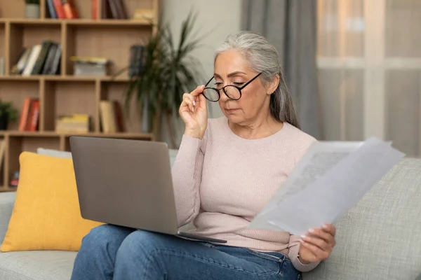 专心致志地忙碌着 戴着眼镜的高加索退休女士 带着文件工作 在客厅的内部纳税 自由自在的空间 在家里远程记账的问题 — 图库照片