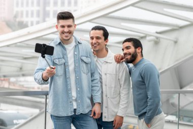 Seyahat eğlencesi. Modern Havalimanı Terminali 'nde uçuş beklerken fotoğraf çeken üç adam cep telefonuyla selfie çekiyor. Bir grup arkadaş birlikte tatile çıkıyor.
