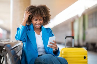 Tren istasyonunda otururken Smartphone 'da kötü mesaj okuyan siyahi kadın, tren istasyonunda tren beklerken cep telefonuyla ilgili sıkıntılar yaşıyor.