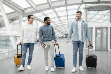 İçinde modern havaalanı terminalinde pasaportları olan seyahat çantalı üç pozitif turist. İstasyonda Erkek Yolcular Grubu 'nun tam uzunlukta çekimi. Tatil ve Ulaşım