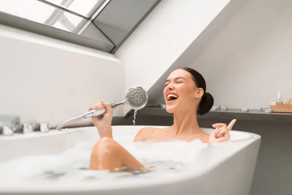 在现代浴室室内 女歌手用泡沫洗澡时唱歌 像麦克风一样抱头洗澡 快乐的女性在家中闭着眼睛享受沐浴 — 图库照片