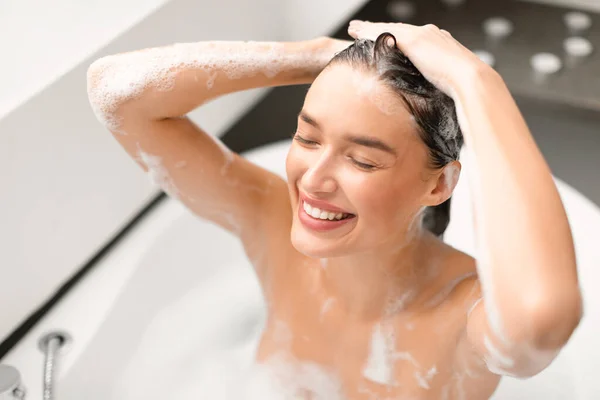 ヘアケア 自宅の近代的なバスルームで目を閉じて洗髪頭の上にシャンプーを適用する陽気女性 ヘアケア化粧品広告コンセプト 選択的フォーカス — ストック写真
