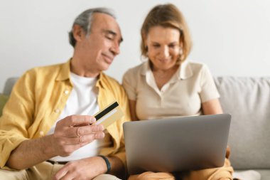 Üst düzey Avrupalı çift dizüstü bilgisayar ve kredi kartı kullanıyor, internetten alışveriş yapıyor veya yemek sipariş ediyor, evdeki kanepede oturuyor, seçici odaklanıyor. Bankacılık için aygıt, alışveriş için satış, reklam ve teklif