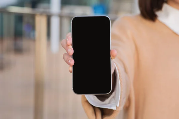 stock image Millennial caucasian woman shows modern smartphone with blank screen, recommends app, blog, website in airport building, cropped. Chat in social networks, ad, online service, booking tickets