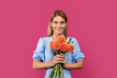 Neşeli orta yaşlı Avrupalı sarışın kadın elinde bir buket çiçek tutuyordu. Mor stüdyo arka planında izole edilmiş kadın gününün tadını çıkarıyordu. Tatil kutlaması, insan duyguları, tebrikler.
