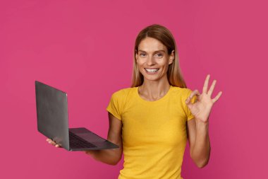 Orta yaşlı Avrupalı sarışın bir kadının dizüstü bilgisayar kullanmasına sevindim. Pembe stüdyo arka planında el izolasyonu ile 