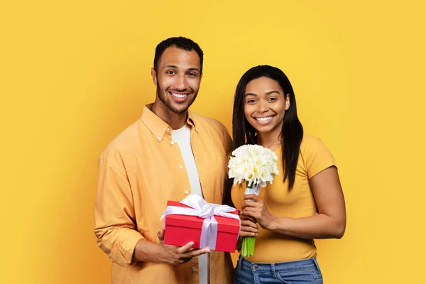 快乐的千年黑人男人送给女人花束和礼品盒 庆祝生日 结婚周年 情人节 在黄色的工作室背景下与世隔绝 — 图库照片