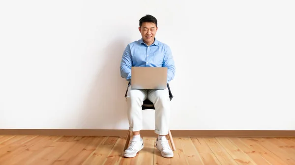 Счастливый Человек Работающий Онлайн Ноутбуке Сидящий Стуле Белой Стены Студии — стоковое фото