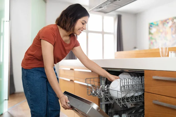 Smiling Young Arab Female Unloading Clean Plates Dishwasher Machine Kitchen — Stok Foto