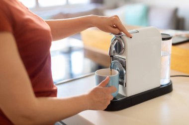Mutfakta espresso makinesi kullanan bir kadın, fincana kahve dolduran, tanınmayan bir kadın tezgahta duran ve sabahları kafein içeceği hazırlayan, modern ev aletlerinin keyfini çıkaran bir kadın.