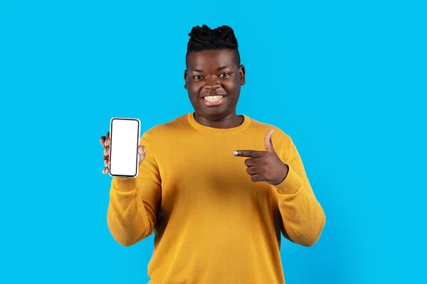 移动广告 快乐的黑人男人手拿着空白智能手机指指点点 微笑着推荐新的应用或网站 而站在蓝色背景的旁边 调侃着 — 图库照片