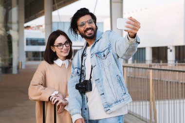 Seyahat blogu. Bin yıllık etnik çeşitliliğe sahip erkek ve kadın turistler akıllı telefondan selfie çekip açık havada video çekiyorlar. Sosyal ağlar, seyahat uygulaması, birlikte tatil.