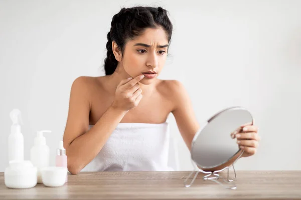 Upset young indian woman touching lips in front of mirror, suffering herpes virus, concerned eastern female having dermatological problem while making beauty routine at home, free space