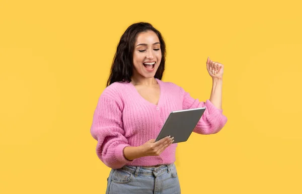 획기적 성공을 축하하기 태블릿으로 타이핑을 승리의 표시를 노란색 스튜디오 배경에서 — 스톡 사진