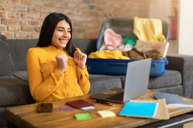 Aşırı neşeli İspanyol bayan dizüstü bilgisayardan ateşli bir tur ayarlıyor, turizm acentesindeki büyük indirimden dolayı heyecanlı, otel rezervasyonu yapan kadın ya da evden uçak bileti alan kadın.