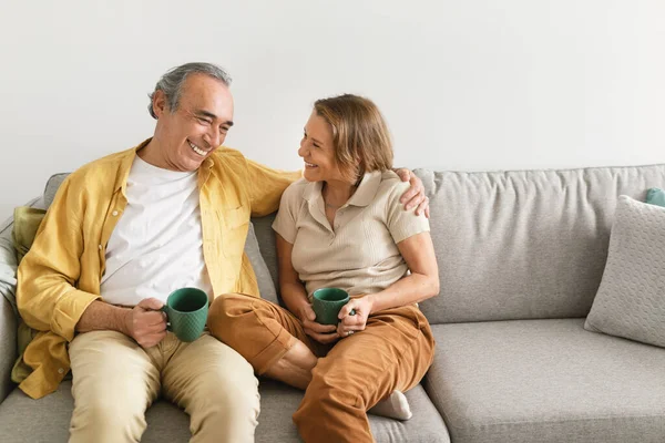 stock image Happy loving spouses drinking coffee and talking, enjoying spending time together, sitting on couch at home, free space. Relationship and communication concept