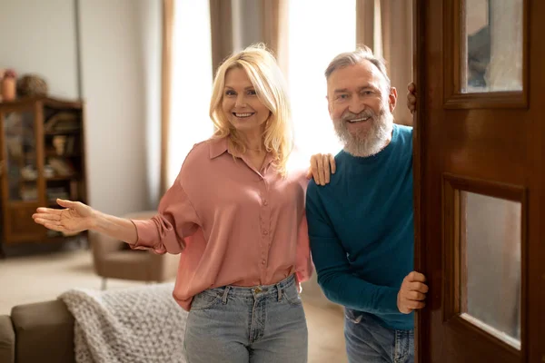 stock image Cheerful Senior Spouses Opening Door Of New Apartment, Welcoming You Smiling To Camera Hugging At Home. Couple Standing In Doors Of Their House. Real Estate Offer And Ownership Concept