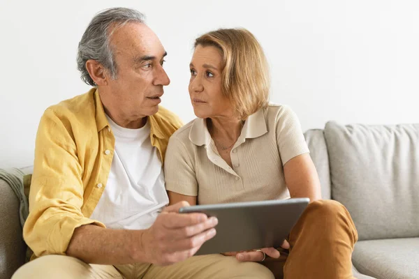 Frightened Retired Couple Using Digital Tablet Looking Each Other Sitting — Stock Photo, Image