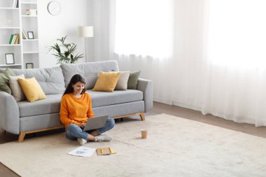 Neşeli, uzun saçlı, sıradan kıyafetler giyen, evde oturan, dizüstü bilgisayar kullanan, çalışan ya da internetten çalışan bilgisayar klavyesinde yazan, kopyalama alanı olan, yüksek açı görüşlü genç bir kadın.