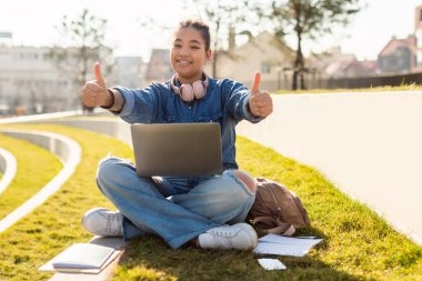 Dizüstü bilgisayarı olan mutlu melez kadın kameraya gülümsüyor, dışarıda parkta oturuyor, boş yer var. Çevrimiçi uzak işi ve uzaktan öğrenme konseptini seviyorum.