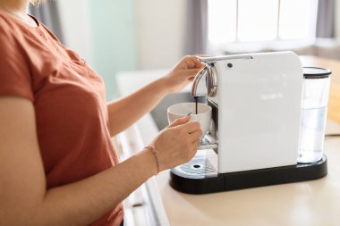 Evdeki mutfakta tanınmayan bir kadının kahve makinesini kullanması, genç bir kadının elinde fincan tutması ve modern aletlerle kafein içeceği doldurması, Millennial Woman 'ın sabah içkisinin tadını çıkarması, kesilmiş görüntüler.